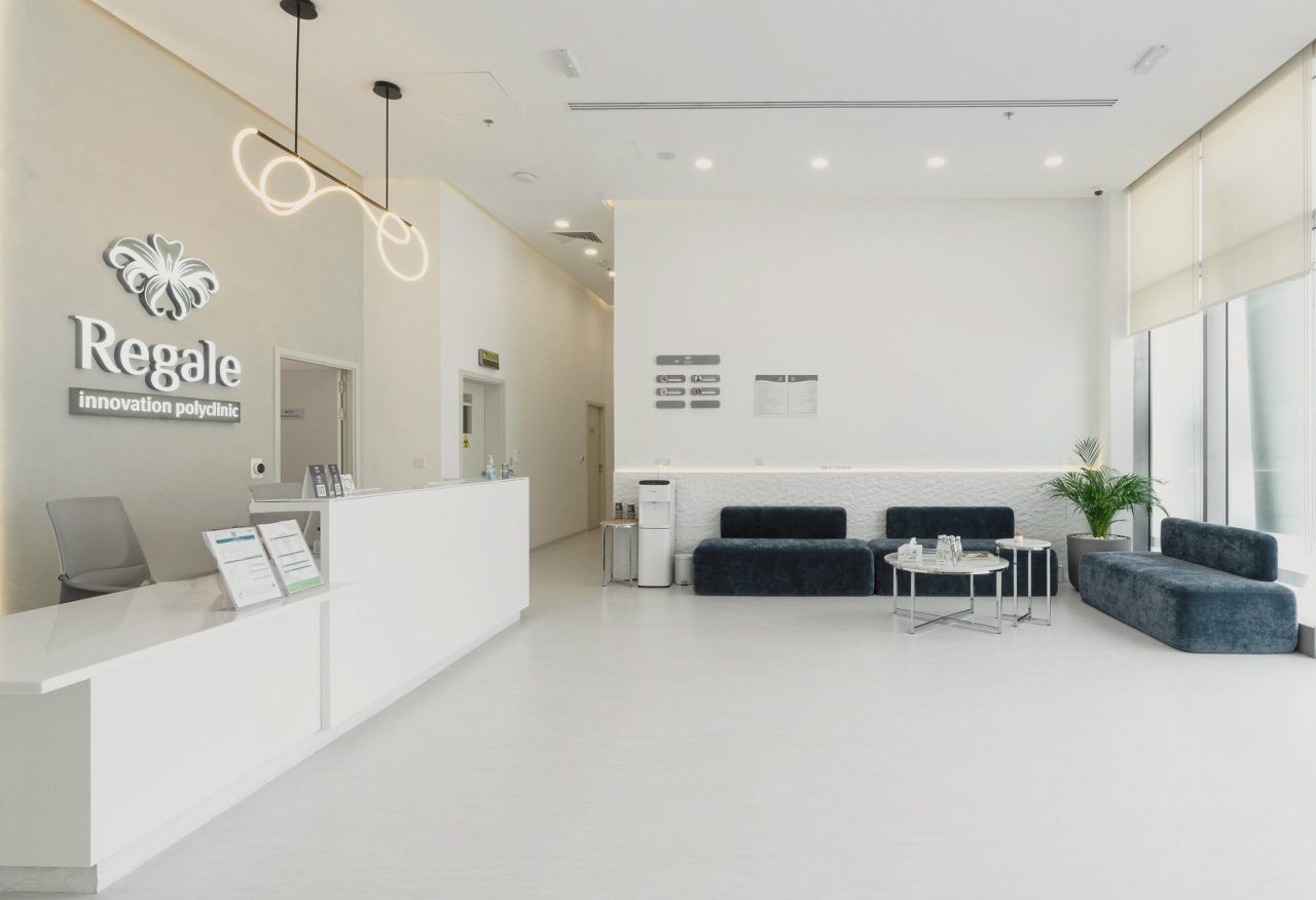 Wide view of the Regal Polyclinic lobby in Dubai, reception counter, ribbon pendant light, male lounge and blue modular seating