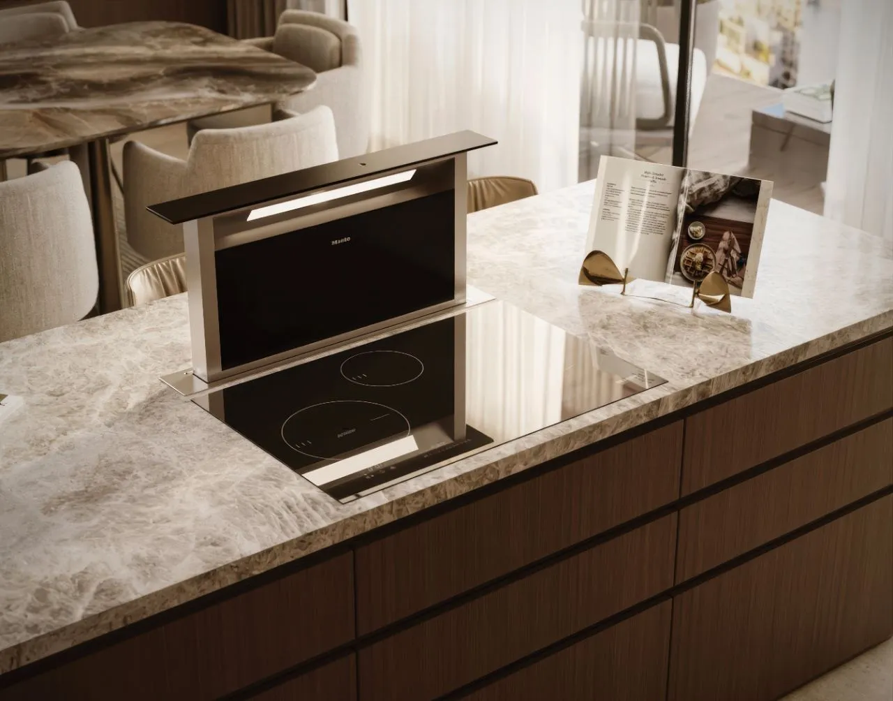 Detail of the quartzite island with a flush induction hob and a rising downdraft extractor beside a cookbook on a brass stand