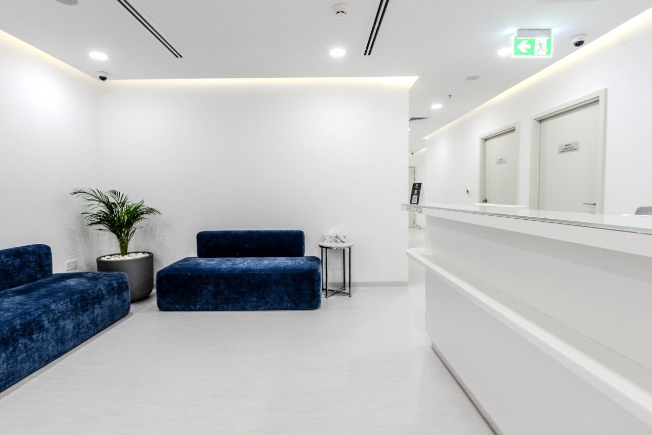 Nurse station counter at Regal Polyclinic beside the waiting lounge, with blue benches, planting and consultation room doors