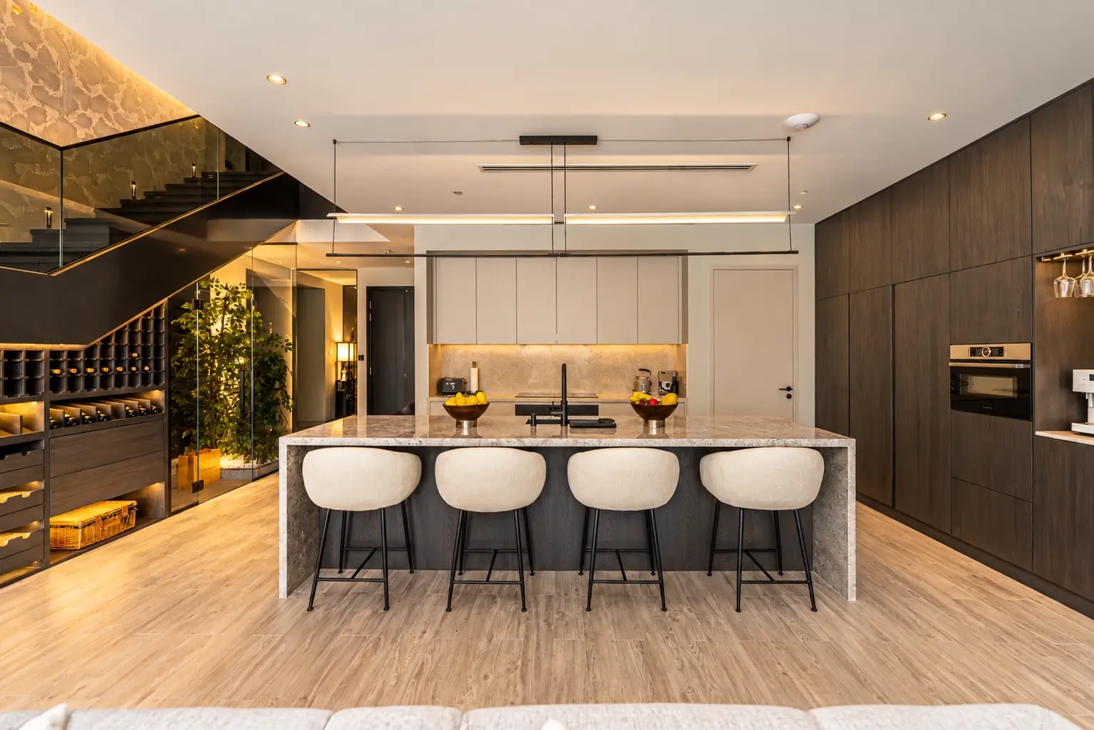 Fitted kitchen with a stone waterfall island, smoked oak full-height cabinetry, integrated ovens and a lit wine store under the stair