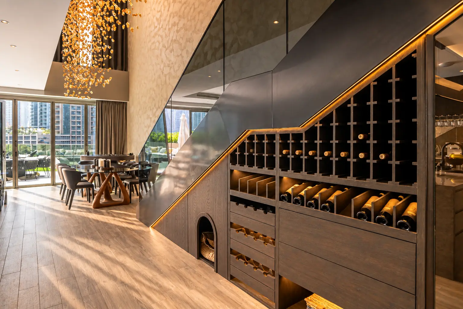 Oak wine store built under a bronze glass staircase, lit along its line, beside a dining table under an amber glass chandelier