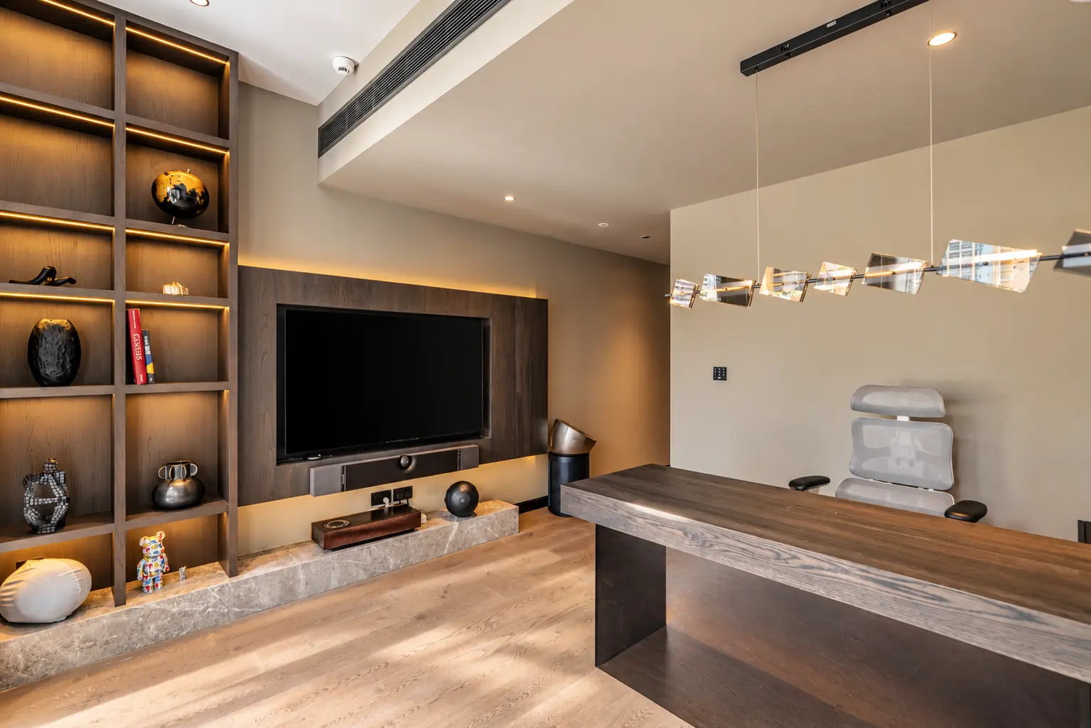 Study with lit smoked oak shelving, an oak-framed media wall on a stone plinth and a solid oak desk under a crystal pendant