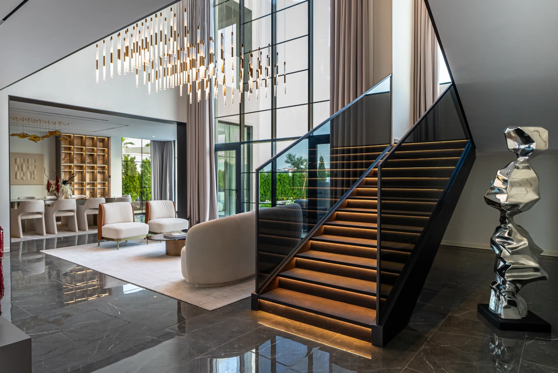 Double-height foyer with cascading linear chandelier and glass staircase