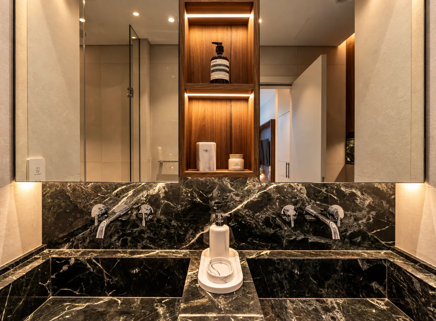 Dark green marble double vanity with wall-mounted taps and a lit walnut niche between mirrors
