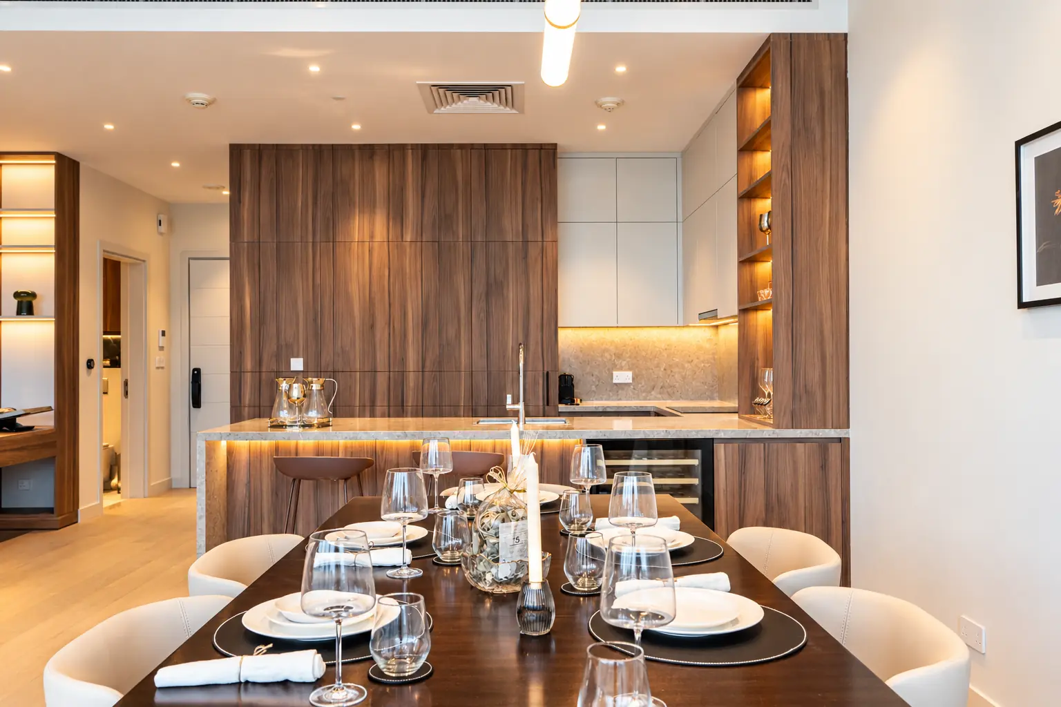 Walnut and cream kitchen with a stone island, bar stools and a set dining table in front