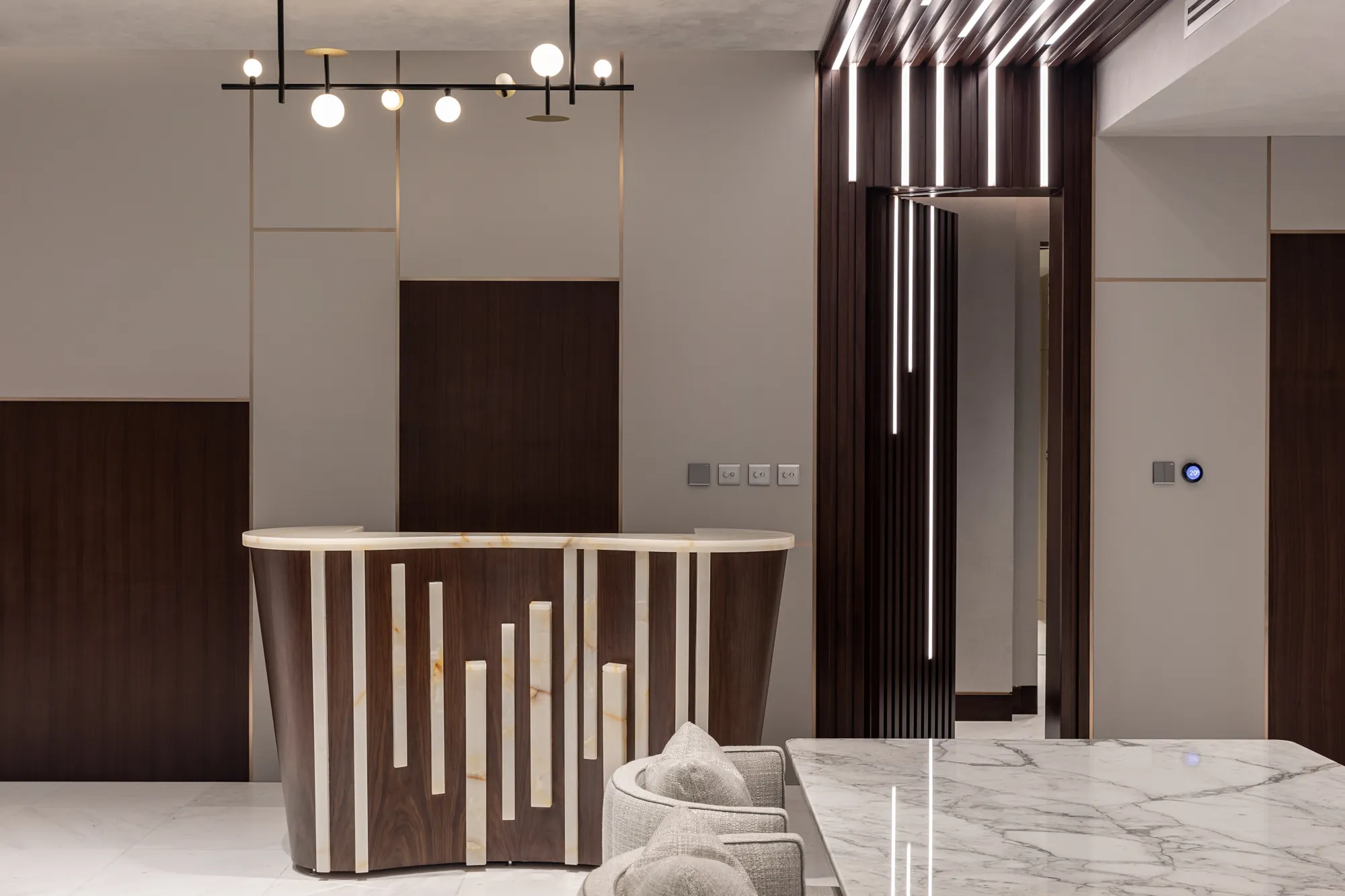 Curved bar counter in walnut with backlit onyx batons and an onyx top, beneath a linear globe pendant and beside a lit walnut slat portal