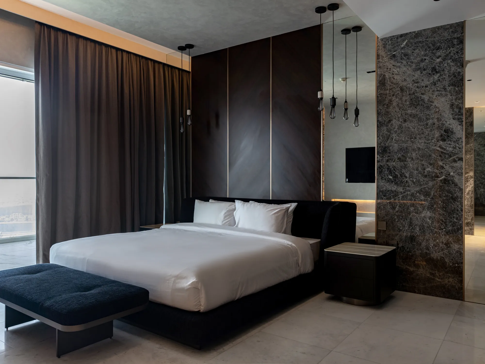 Master bedroom with dark timber wall panels and metal inlays, an upholstered bed, pendant bulbs and a full-height grey marble wall