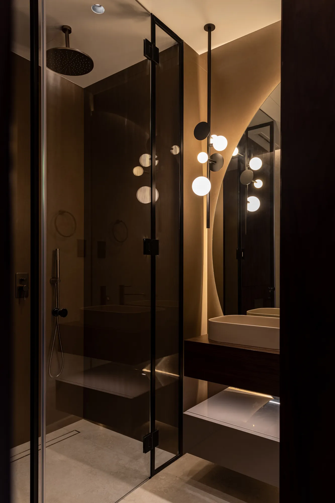 Guest shower in smoked glass with black frames beside a floating vanity and a round backlit mirror