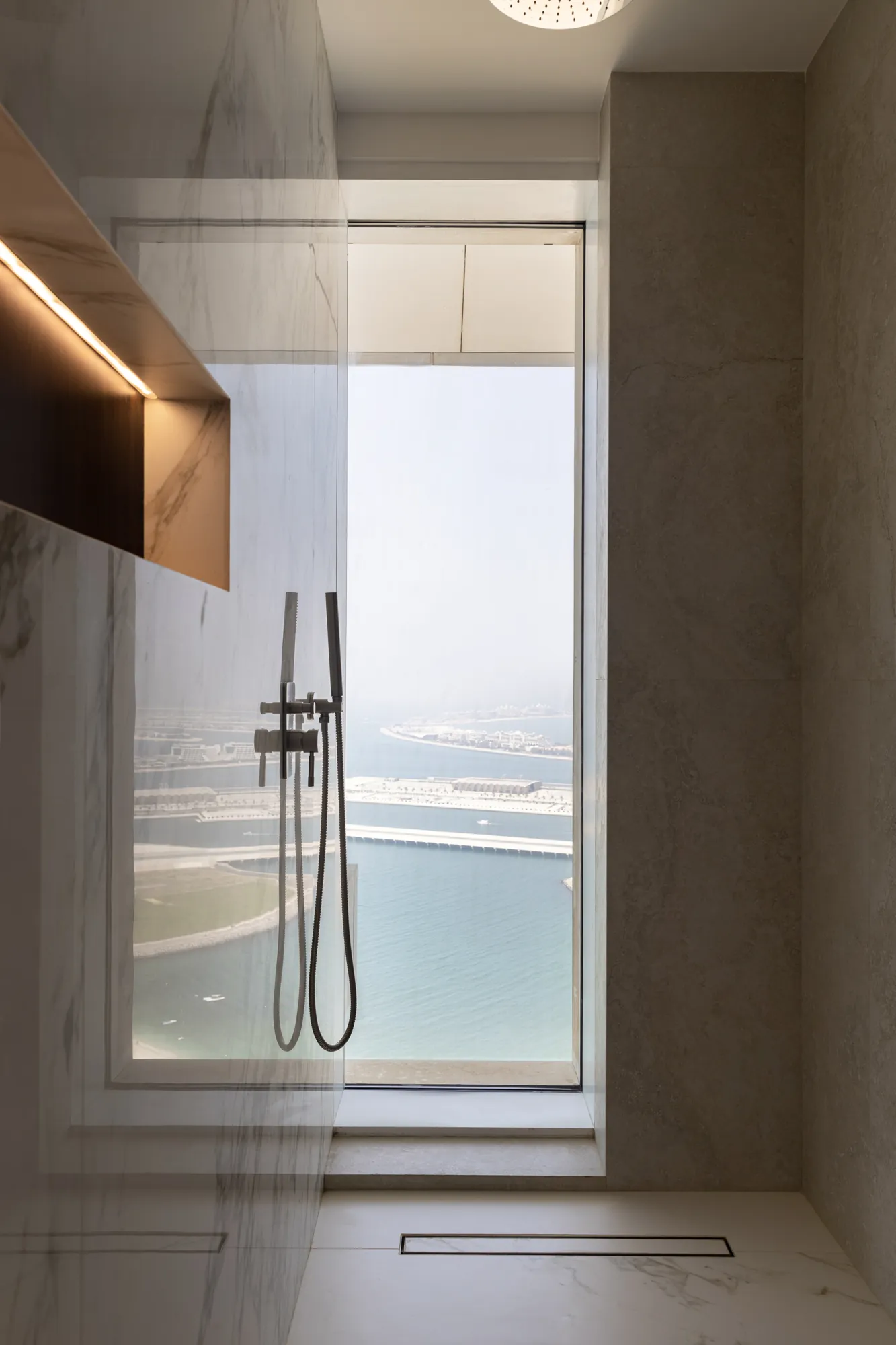 Walk-in shower lined in marble-effect stone with a full-height window looking out over the sea and the Palm