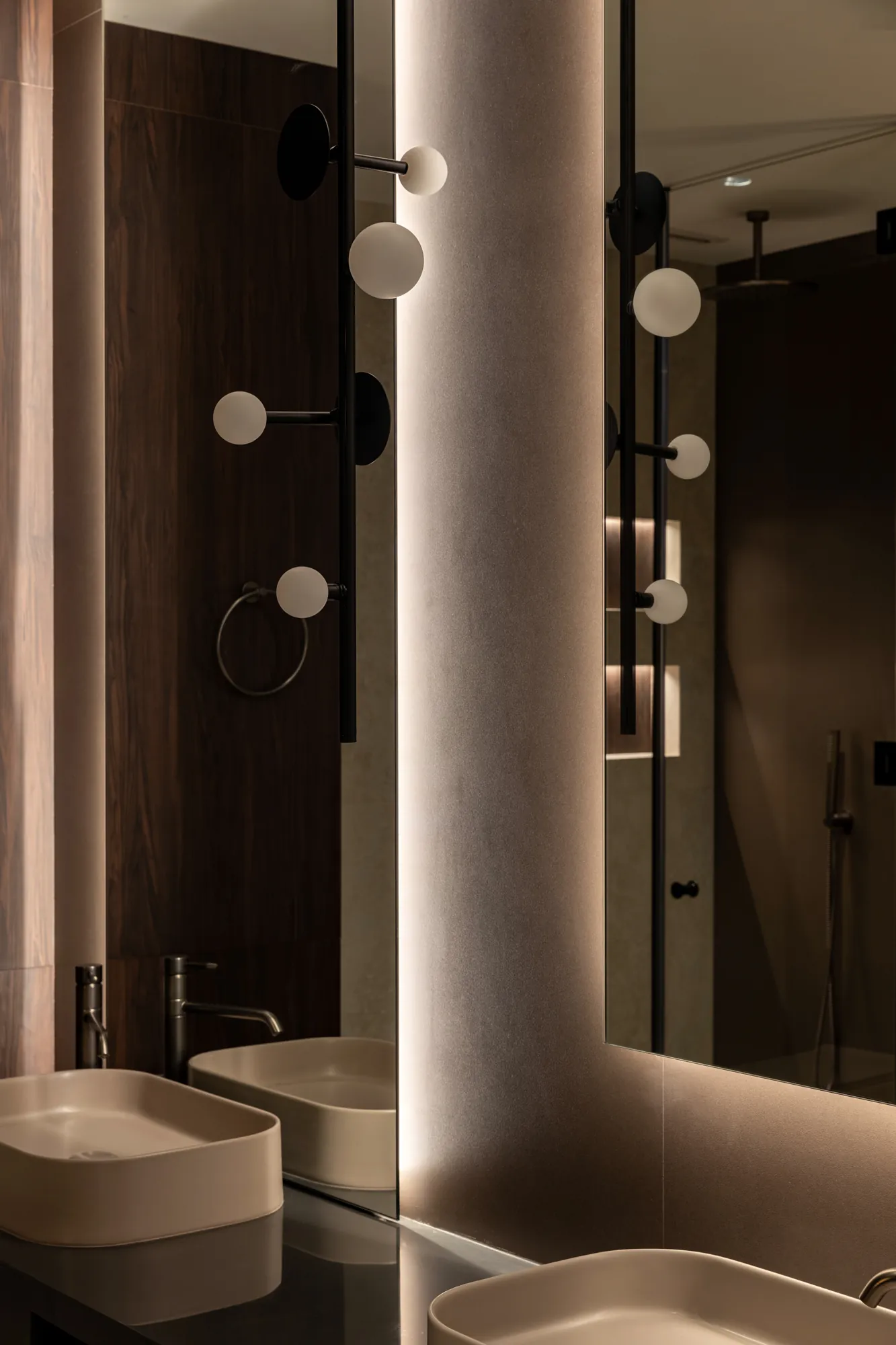 Twin vessel basins beneath backlit mirrors with a black rod sconce of frosted globes