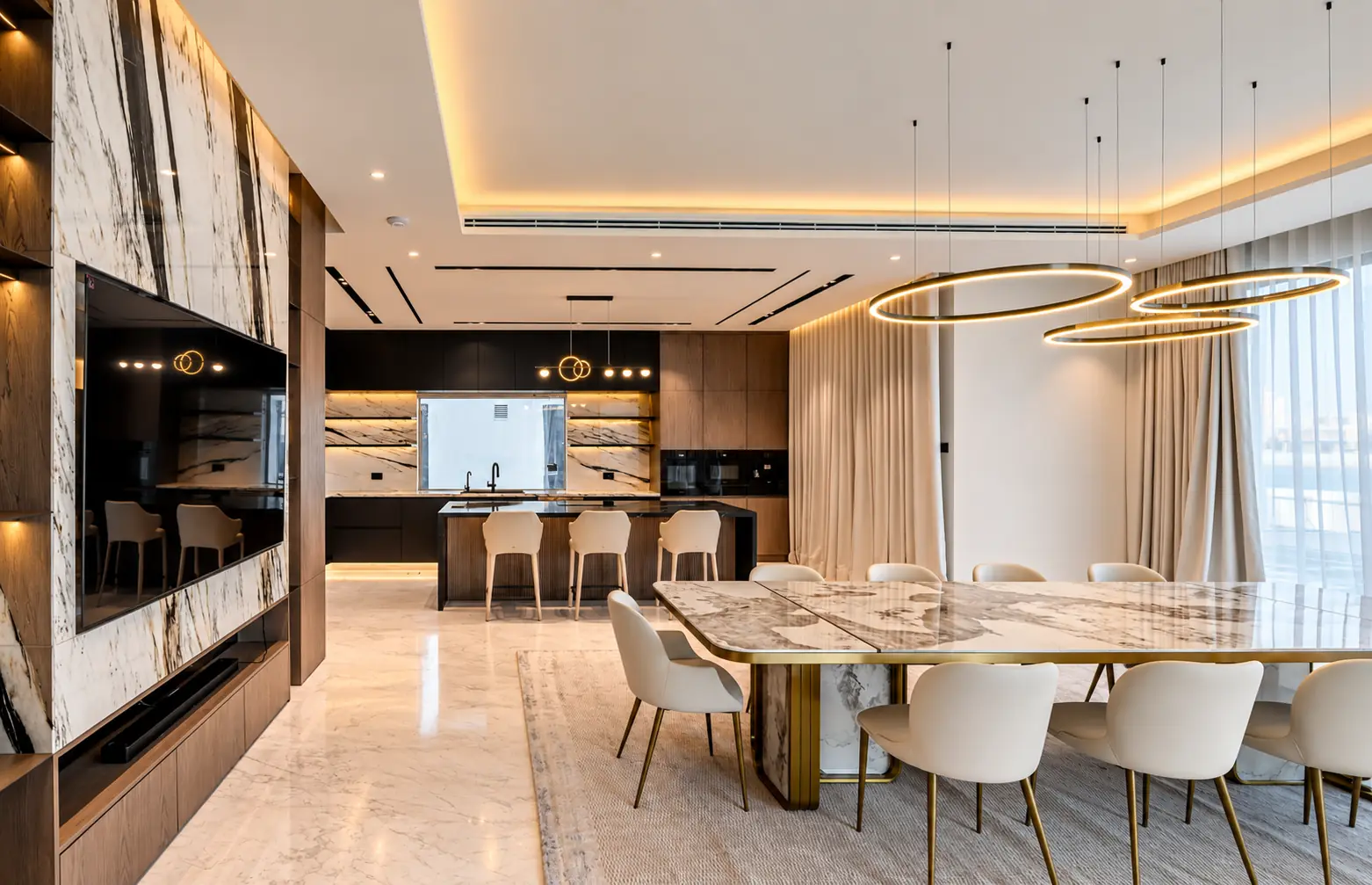 Open-plan dining with a marble-topped table under floating ring pendants, looking through to the walnut and black kitchen