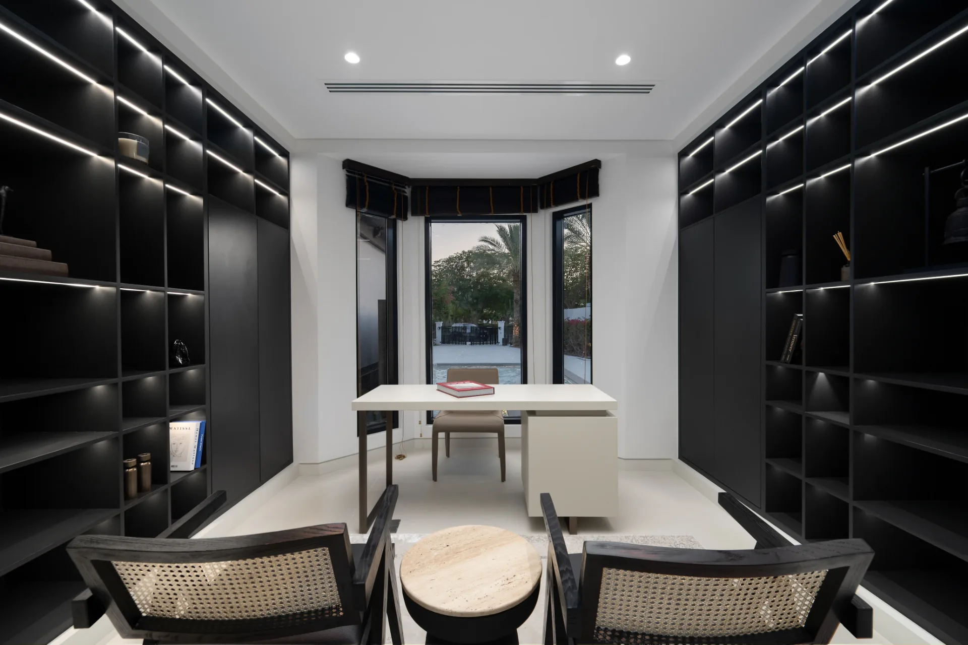 Study with black library shelving and white desk overlooking the pool