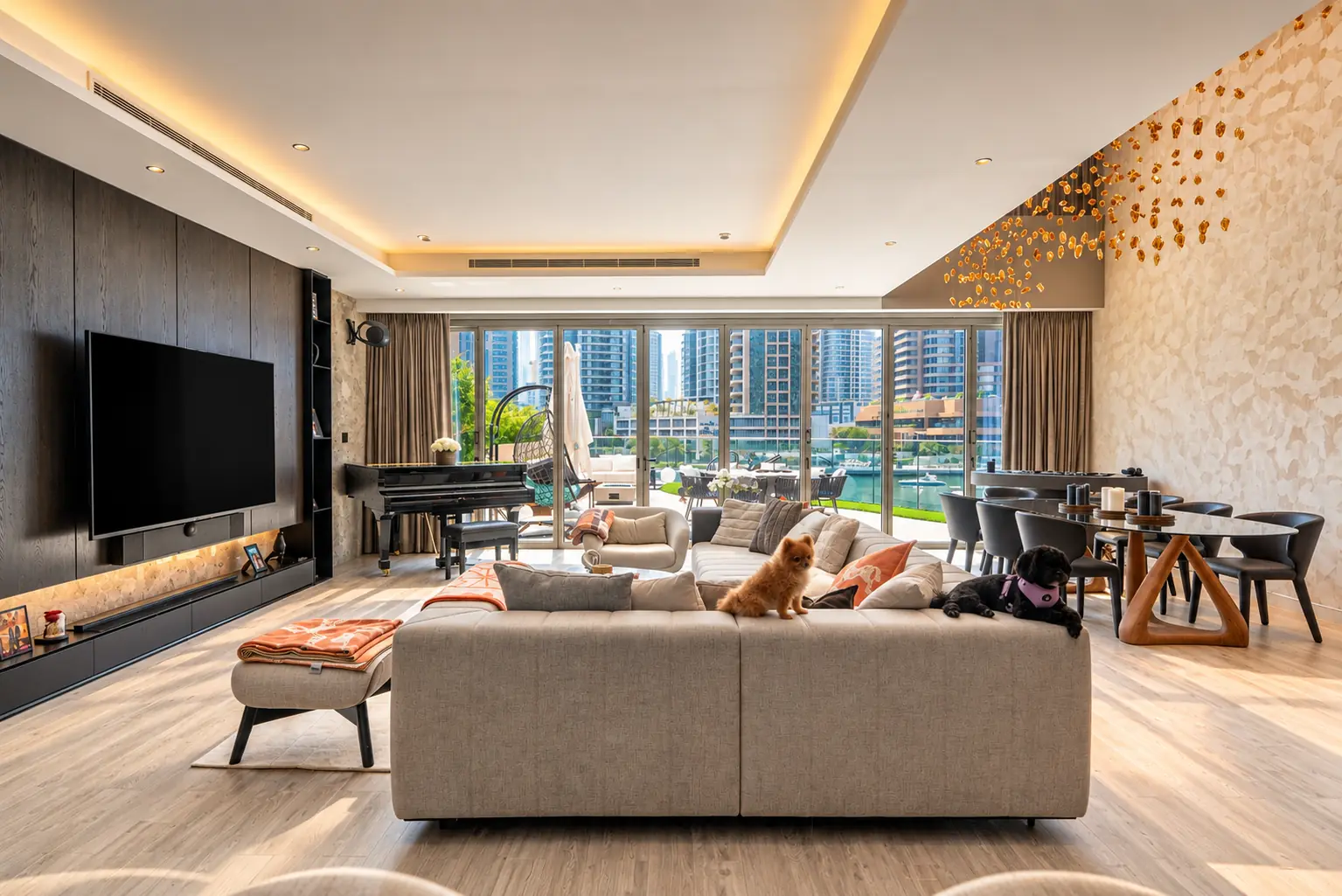 Open-plan living room in a Dubai marina-front villa with a stone-grey sectional sofa, dark oak media wall, grand piano, glass dining table and floor-to-ceiling glazing onto the water